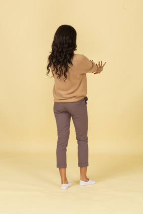Three-quarter back view of a dark-skinned young female outstretching hands
