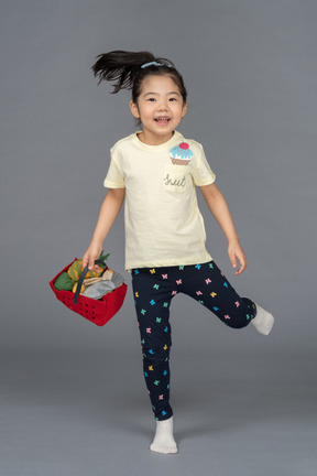 Portrait of a little girl skipping on one leg while holdin a shopping basket