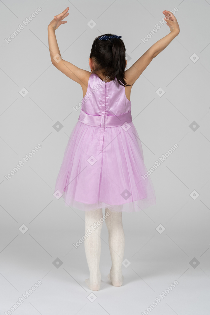 Vista trasera de una niña con las manos en alto