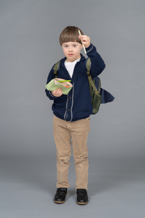 Portrait of a little boy with a backpack holding up a pencil