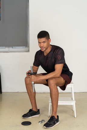 Young man in sports clothes sitting on white stool