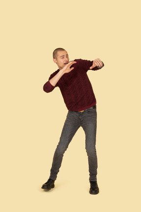 Front view of a scared young in red pullover raising his hands