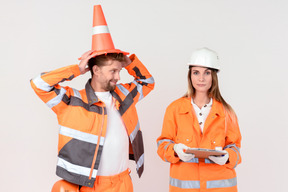 Female road worker standing next to male colleague with cone on his head