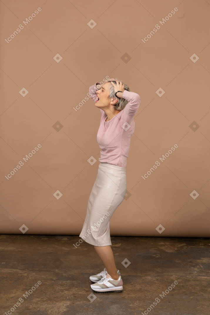 Vista lateral de uma mulher emocional em roupas casuais em pé com as mãos atrás da cabeça