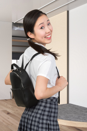 A young girl in a school uniform holding a backpack