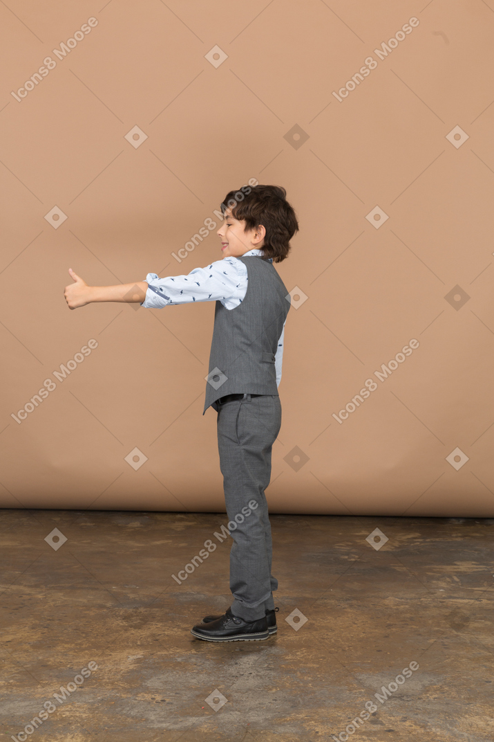 Вид сбоку на мальчика в сером костюме, показывающего большой палец вверх