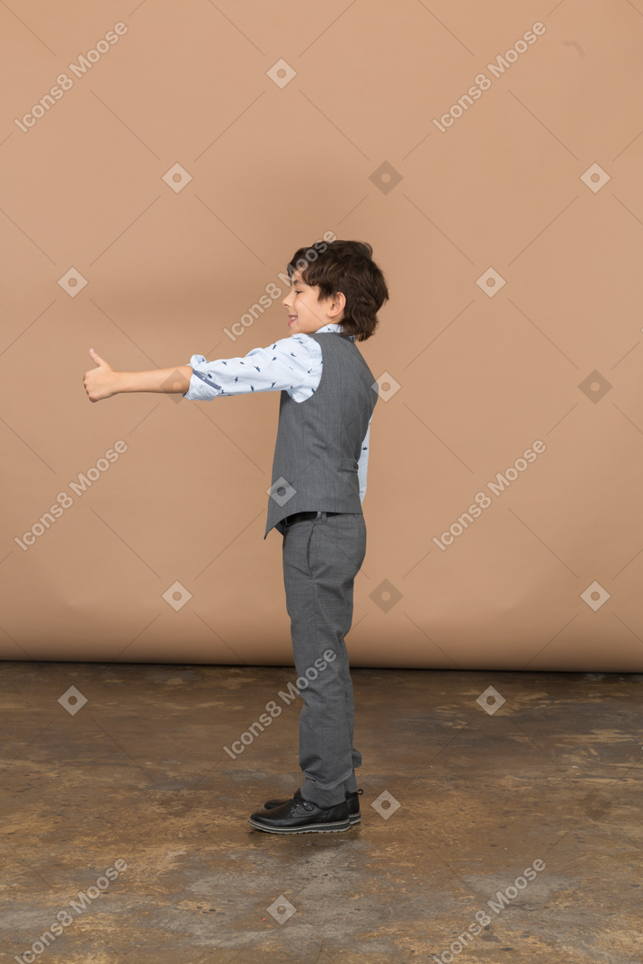 Side view of a boy in grey suit showing thumb up