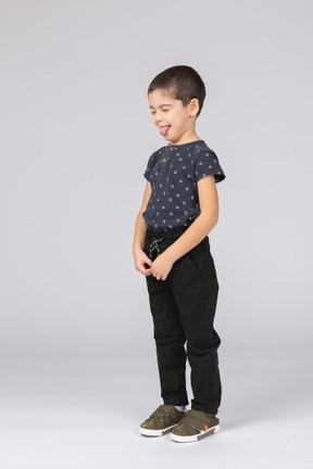 Vue latérale d'un garçon mignon dans des vêtements décontractés montrant la langue