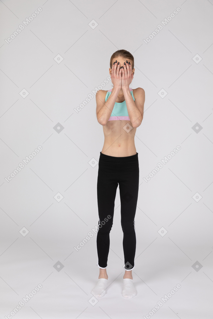 Vista frontal de uma adolescente em roupas esportivas escondendo o rosto