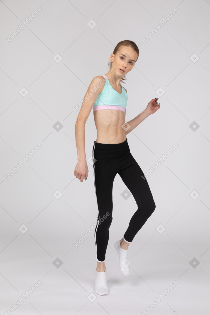 Three-quarter view of a teen girl in sportswear bending knee and looking at camera