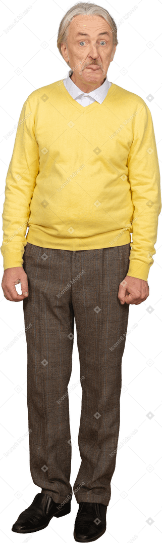 Vue de face d'un vieil homme dans un pull jaune montrant la langue
