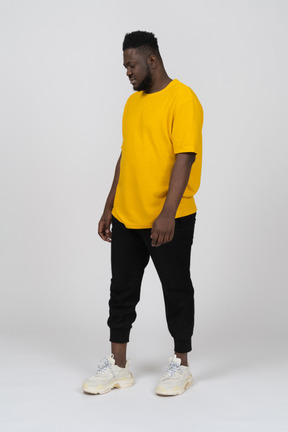 Three-quarter view of a young dark-skinned man in yellow t-shirt standing still