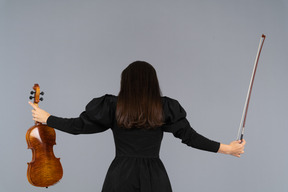 Vista de trás de uma violinista em vestido preto estendendo as mãos