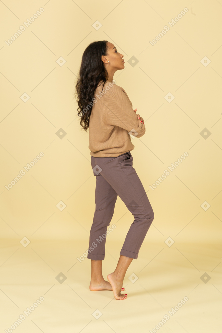 Vista lateral de una joven mujer de piel oscura cruzando los brazos