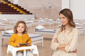 Little girl sitting in a chair with tablet next to woman