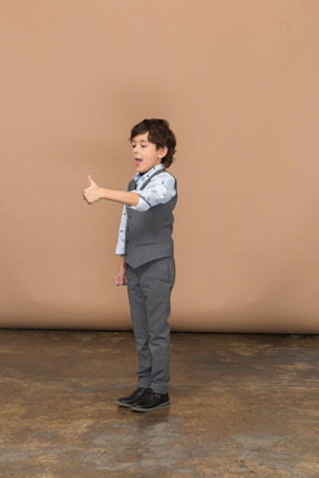 親指を上に表示している灰色のスーツを着た少年の側面図