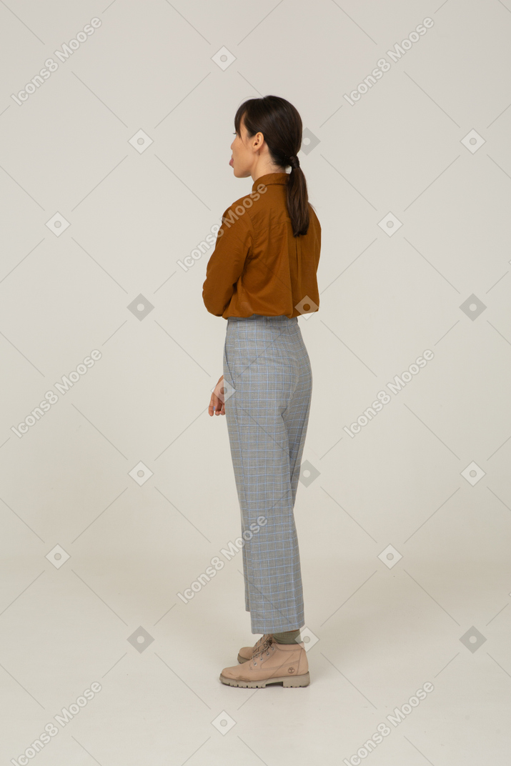 Three-quarter back view of a young asian female in breeches and blouse touching arm and showing tongue
