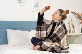 Side view of an ill young lady in pajamas with pills wrapped in checked blanket in bed