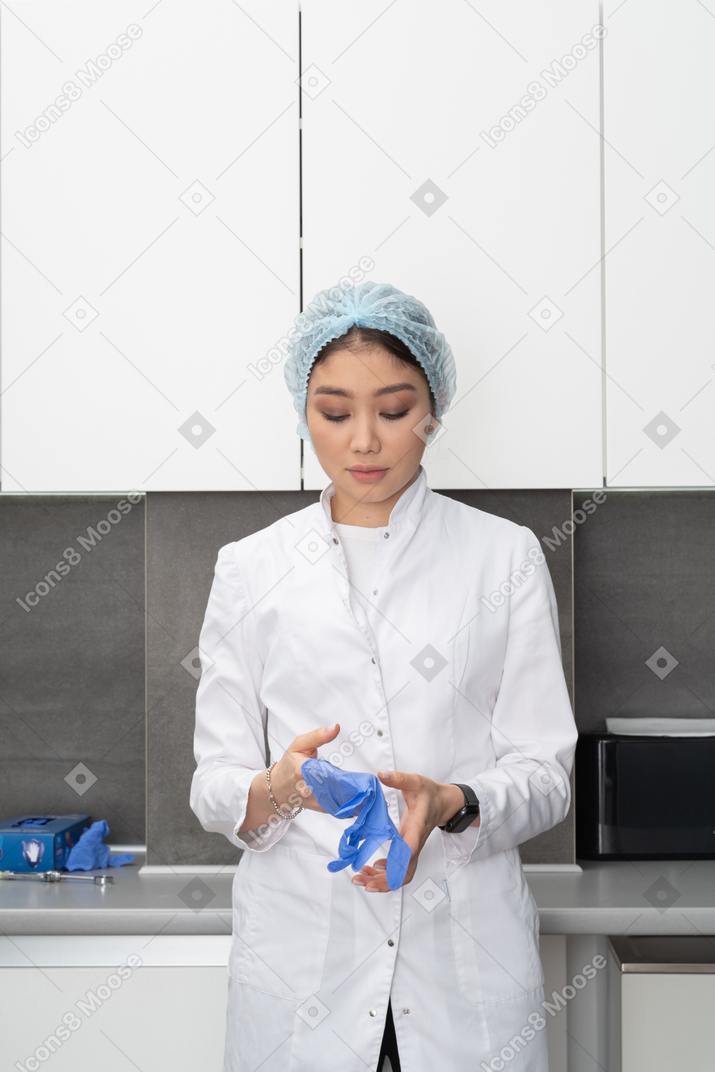 Front view of a young female doctor in hat putting on protective gloves