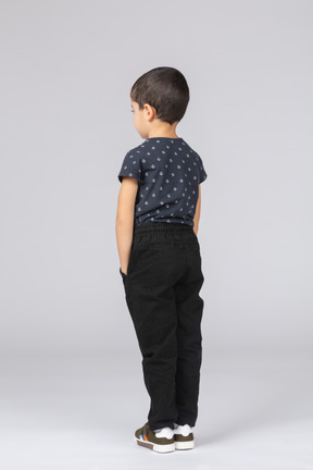 Вид сзади симпатичного мальчика в повседневной одежде, позирующего с руками в кармане