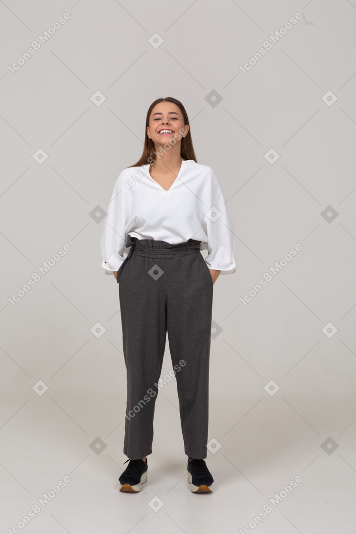 一位身着办公室服装、双手插口袋的微笑年轻女士的前视图