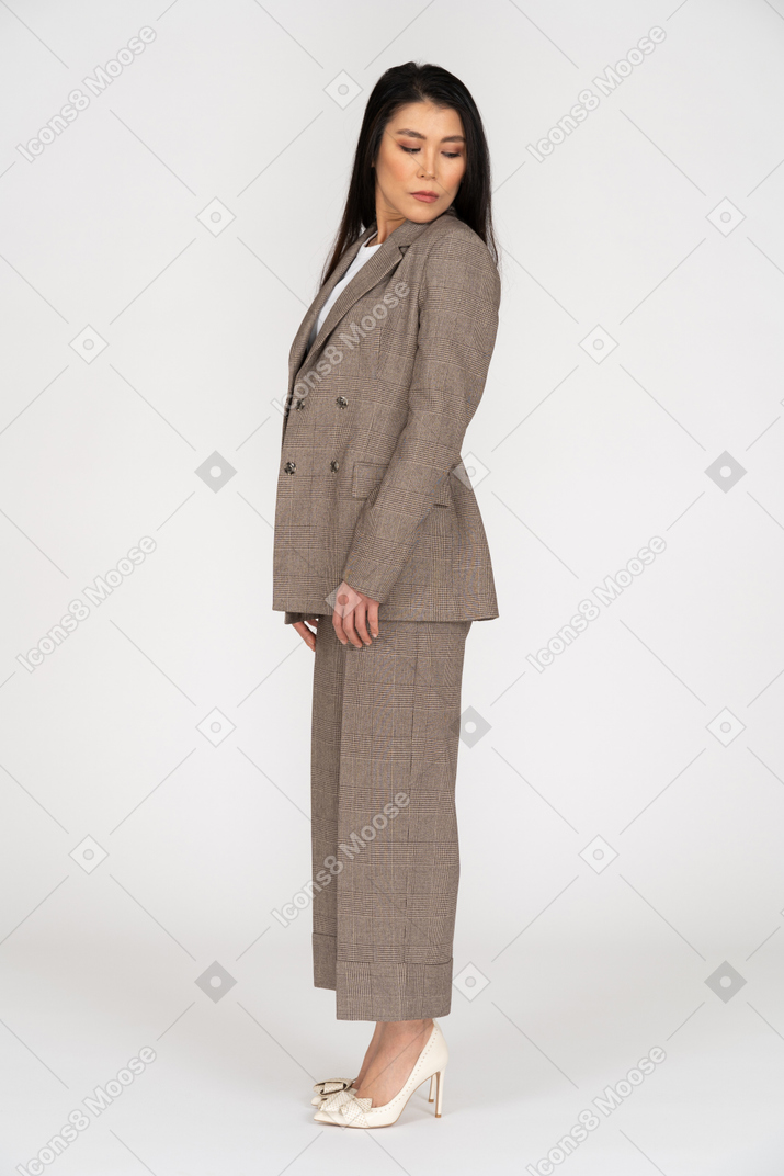 Side view of a young lady in brown business suit turning head and looking down