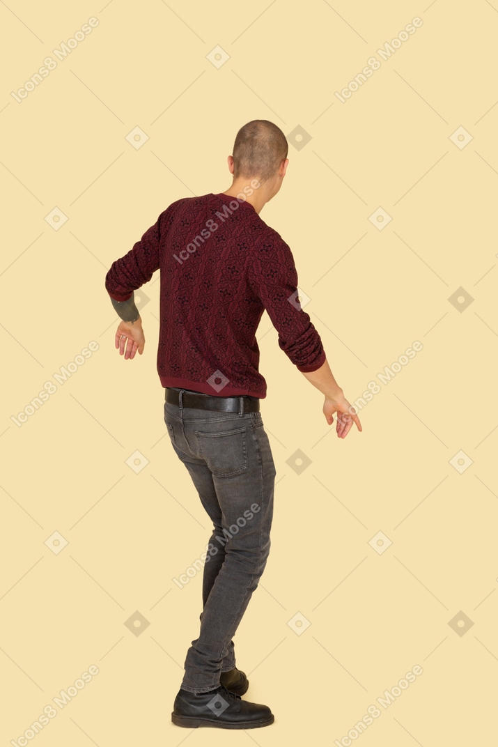 Vista posteriore di tre quarti di un giovane che balla vestito con un pullover rosso
