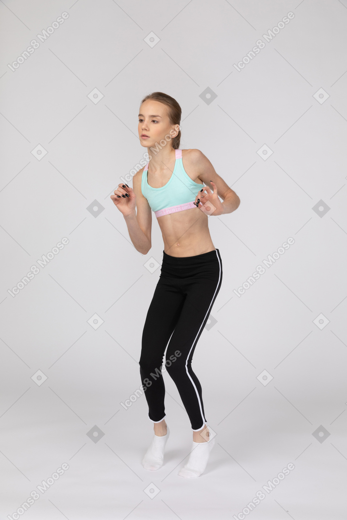 Vista de tres cuartos de una jovencita en ropa deportiva levantando las manos mientras está de puntillas