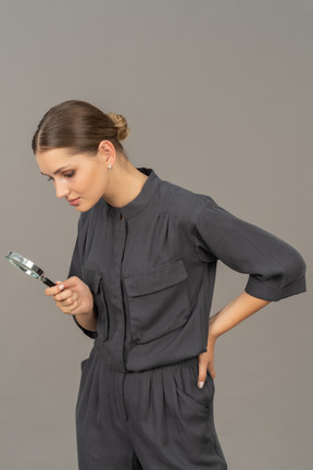 Three-quarter view of a young woman in a jumpsuit holding a magnifying glass