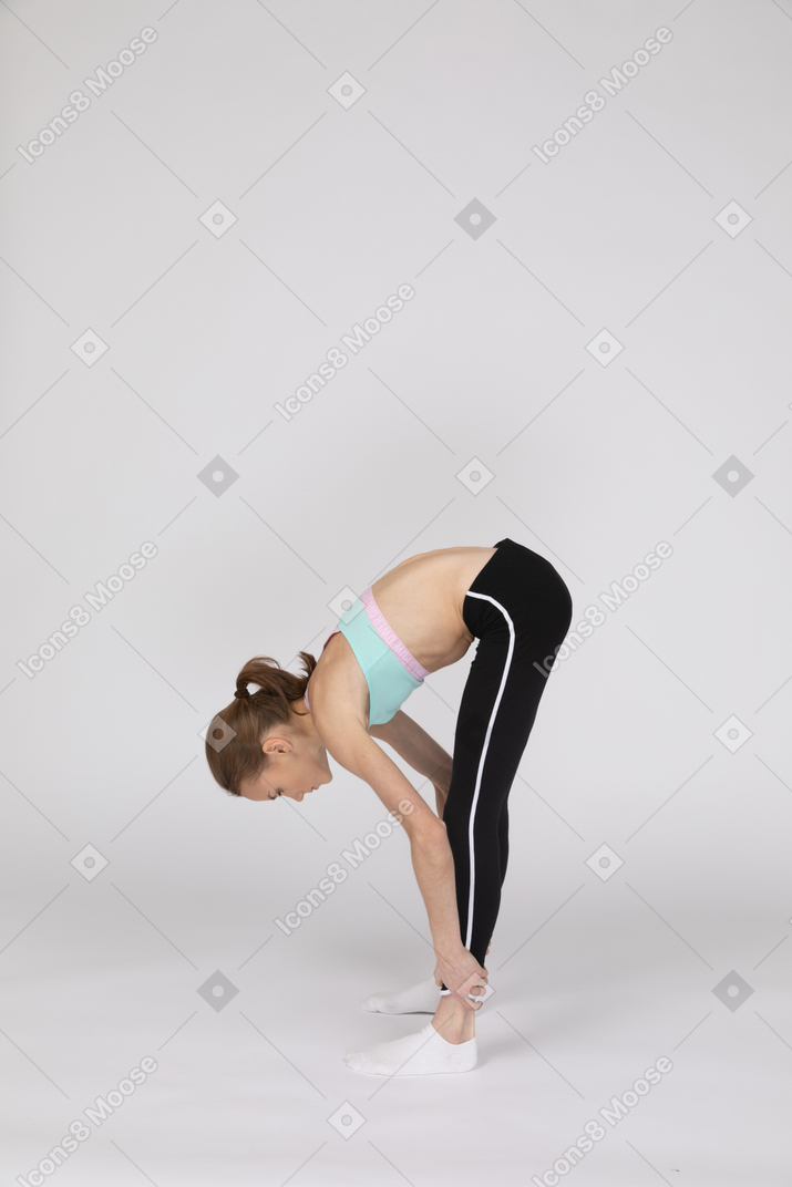 Vista laterale di una ragazza adolescente in abiti sportivi accovacciata e mettendo le mani sui fianchi