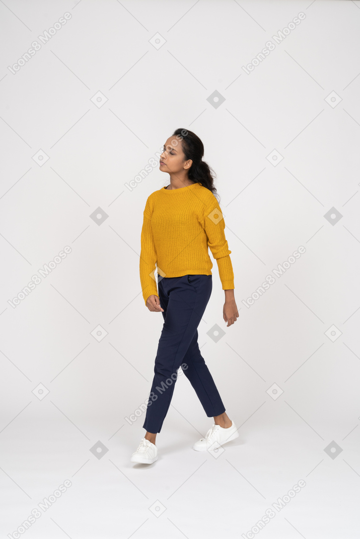 Vista frontal de una niña en ropa casual caminando y mirando hacia arriba