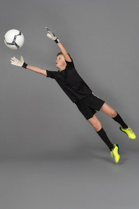Side view of a kid boy goalkeeper jumping and outstretching hands to catch the ball