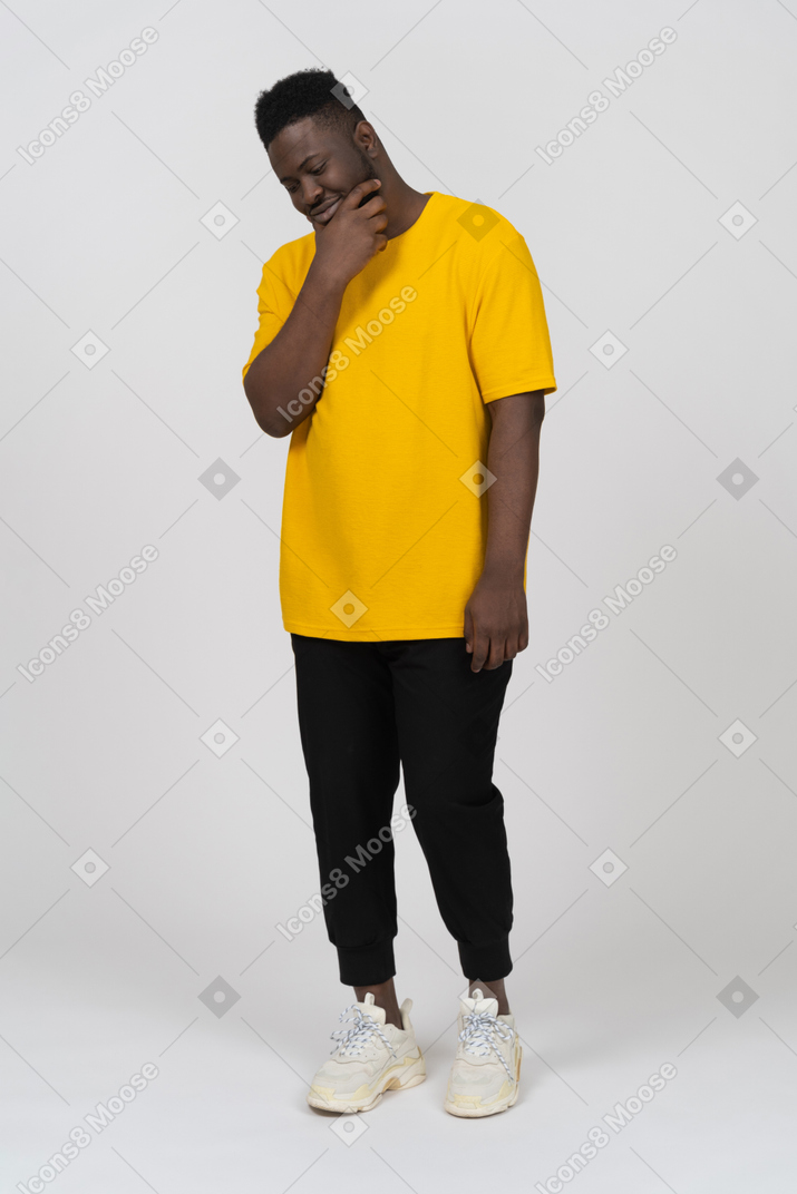 Dreiviertelansicht eines ratenden jungen dunkelhäutigen mannes in gelbem t-shirt, der das kinn berührt