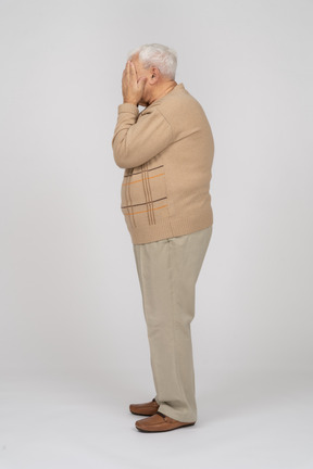 Side view of an old man in casual clothes covering face with hands