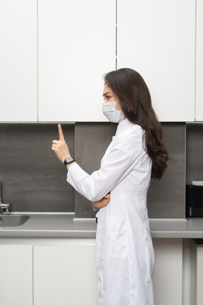 Side view of a serious female doctor in a mask pointing finger