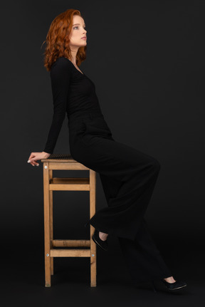 A side view of the sexy woman sitting on the wooden chair and looking to the right side