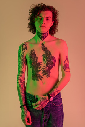 A tattooed male holding his jeans in red and green light