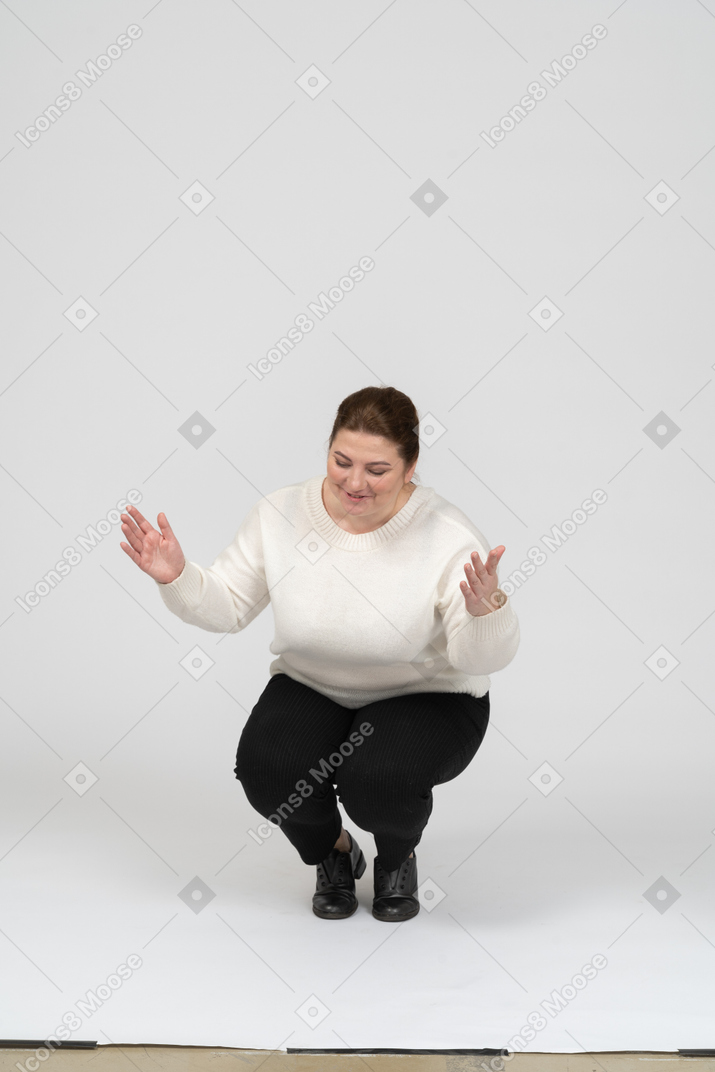 Front view of a happy plump woman in casual clothes squatting