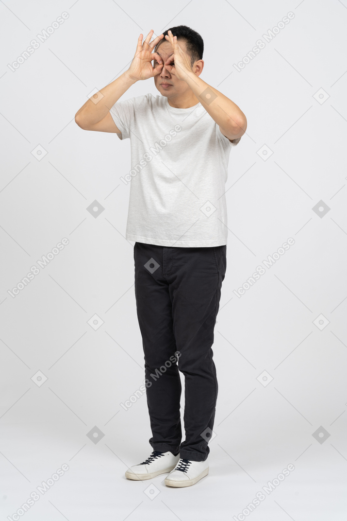 Three-quarter view of a man in casual clothes looking through imaginary binoculars