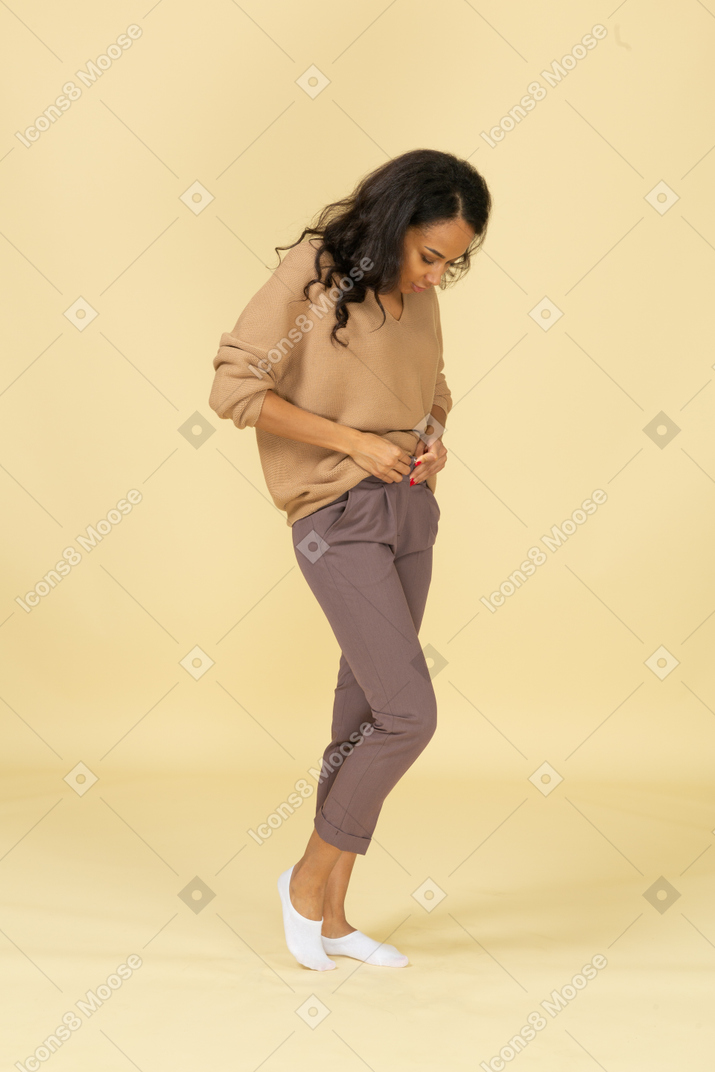 Three-quarter view of a dark-skinned young female zipping up her pants