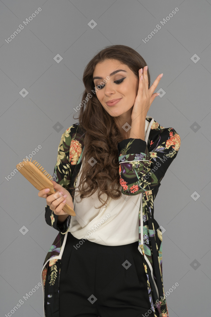 Cheerful smiling woman holding hair brush and  adjusting her brown hair