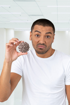 Man in a white t-shirt is holding a small coronavirus molecule