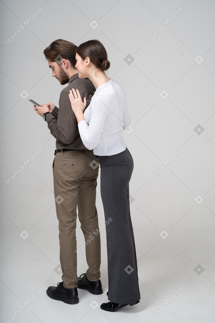 Вид сзади в три четверти молодой леди, подглядывающей в телефон своего парня
