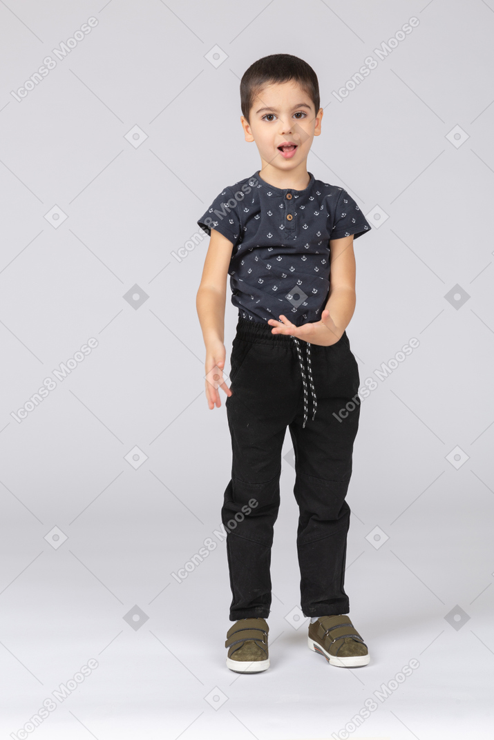 Front view of a cute boy standing with extended arm and looking at camera