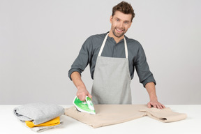 Smiling young househusband ironing clothes