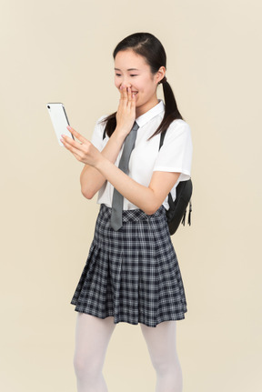 Laughing asian school girl looking at smartphone