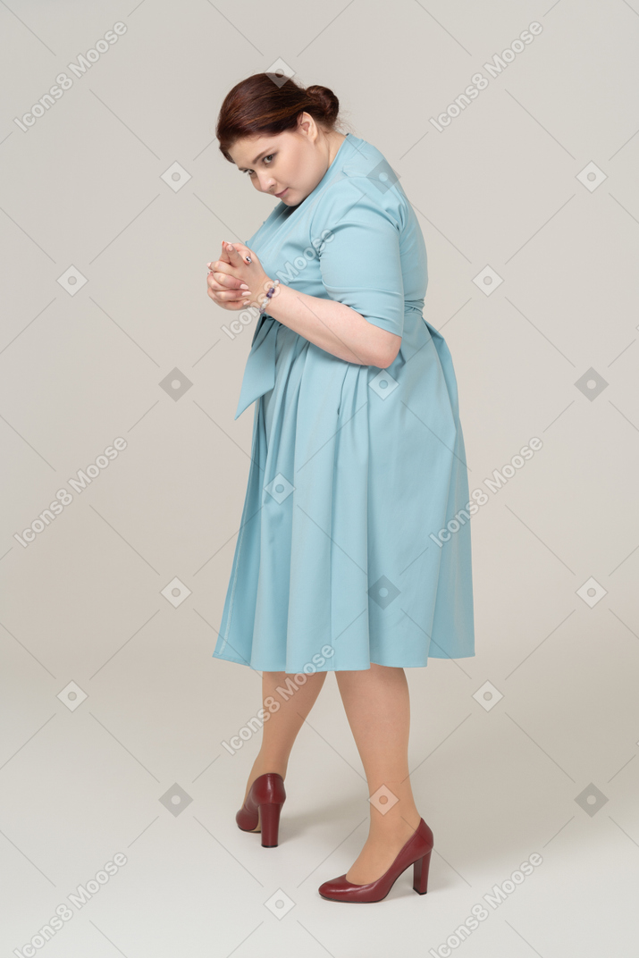 Vista lateral de uma mulher de vestido azul mostrando a arma com os dedos