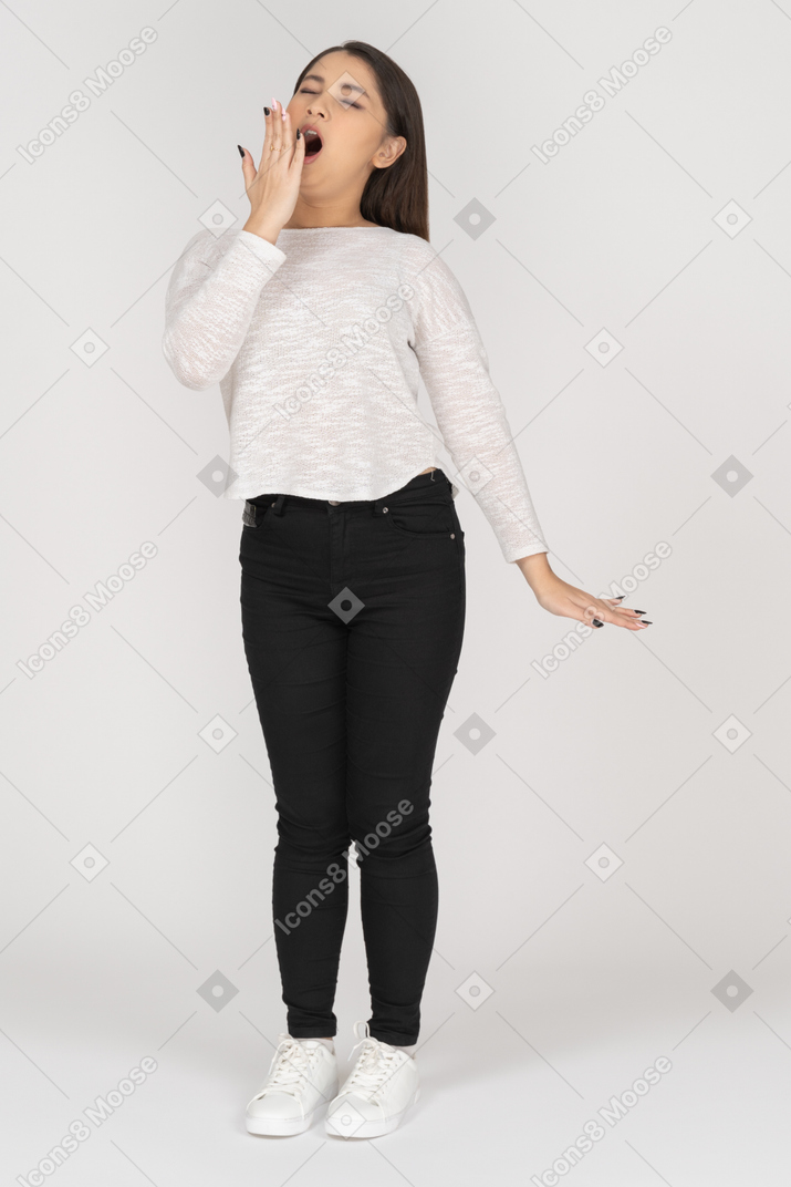 Three-quarter view of a yawning young indian female in casual clothes hiding her mouth