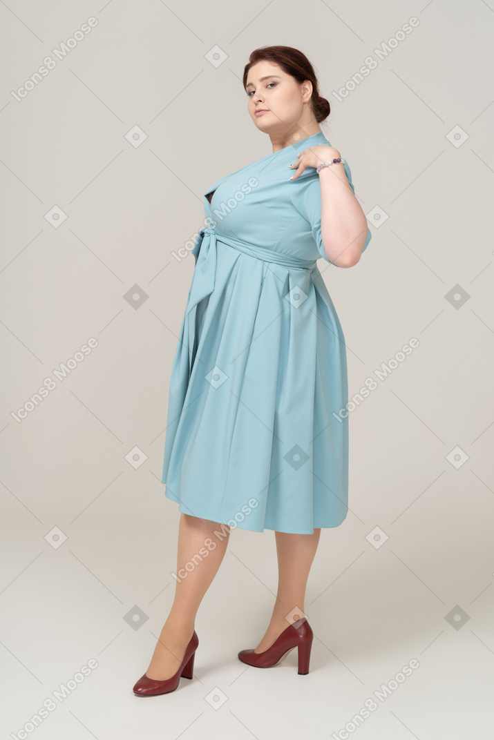 Вид сбоку женщины в синем платье позирует с руками на плечах