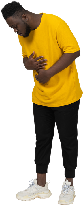 Vista di tre quarti di un giovane uomo dalla pelle scura in maglietta gialla che tocca lo stomaco e guarda in basso